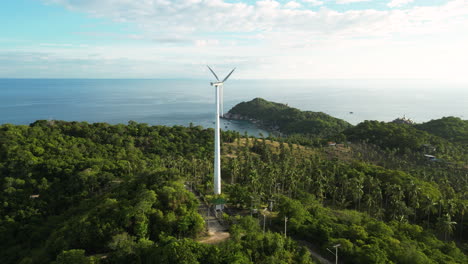 aerial of isolated windmill wind turbine for renewable clean green energy supply on top of green hill surrounded of unpolluted vegetation pure nature and with ocean sea