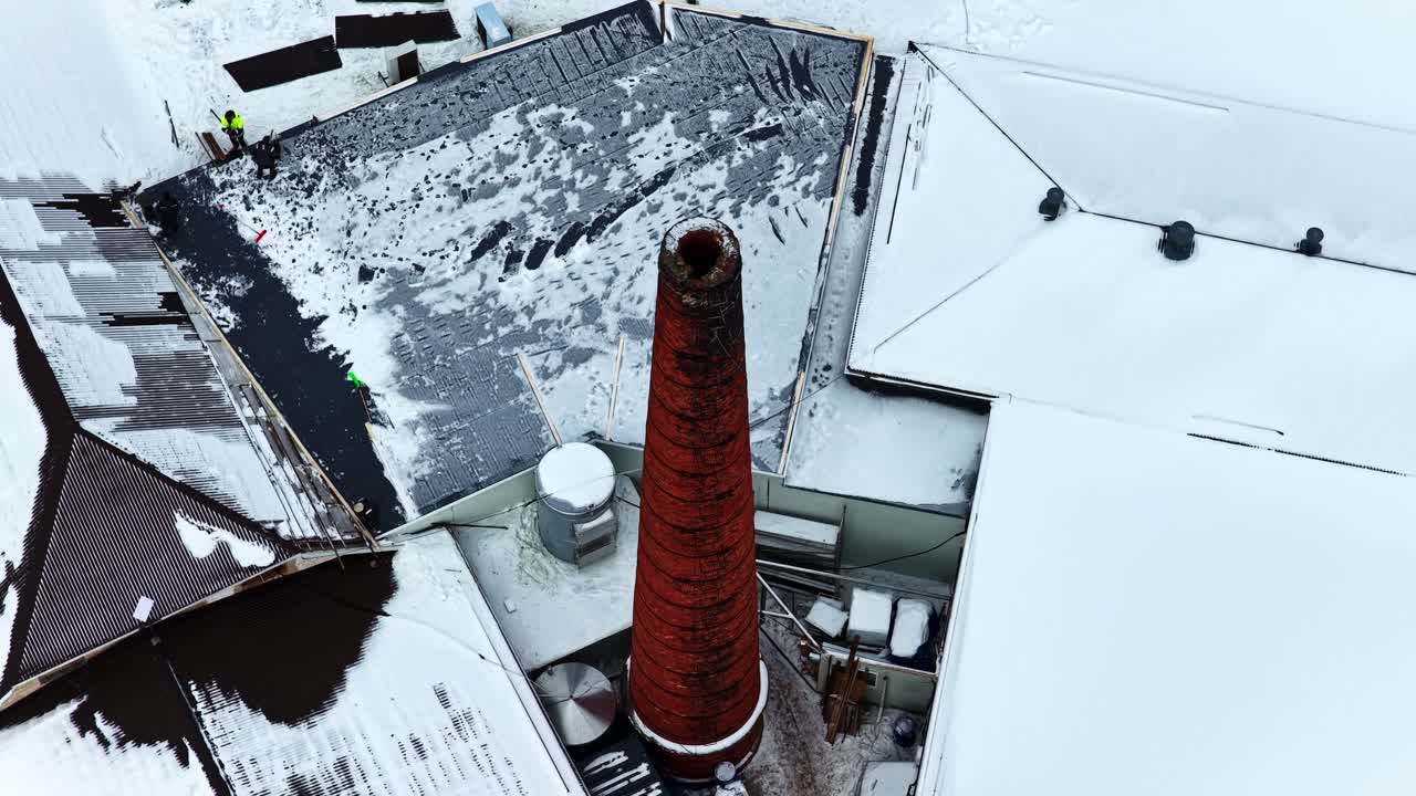 Industrial facility chimney on snowy roof during winter maintenance roof repairs