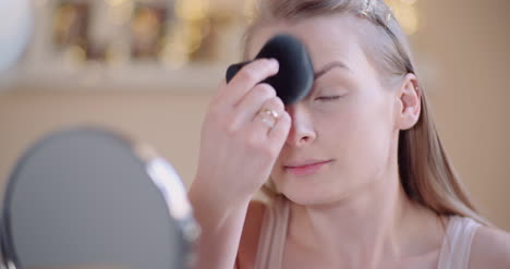 young woman doing makeup in front of mirror at home 1