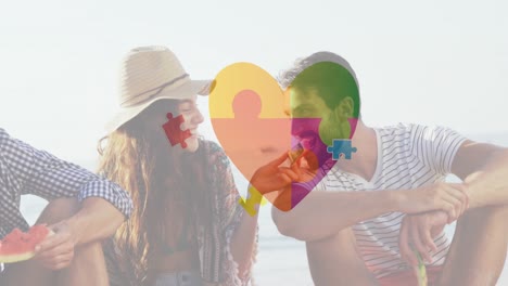 Animation-of-colourful-puzzle-pieces-heart-over-happy-friends-at-summer-beach-party