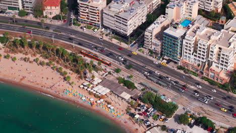 Toma-Aérea-En-Círculos-De-Una-Línea-De-Tranvía-Y-Una-Carretera-Junto-A-La-Playa-De-Atenas,-Grecia.