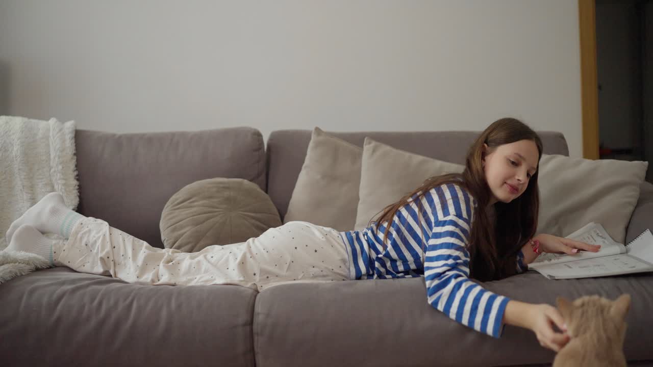 Girl lying on sofa with cat and book