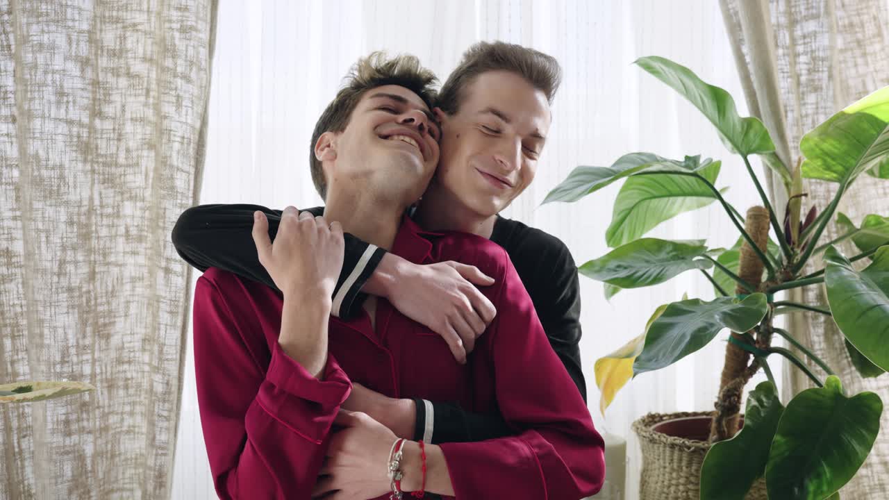 Casal gay jovem feliz se abraçando e sorrindo em casa