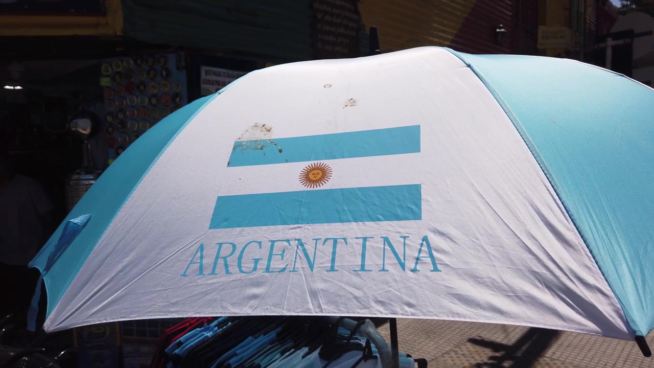 Ombrello con bandiera argentina in primo piano, ripresa a mano su una strada cittadina a Buenos Aires.