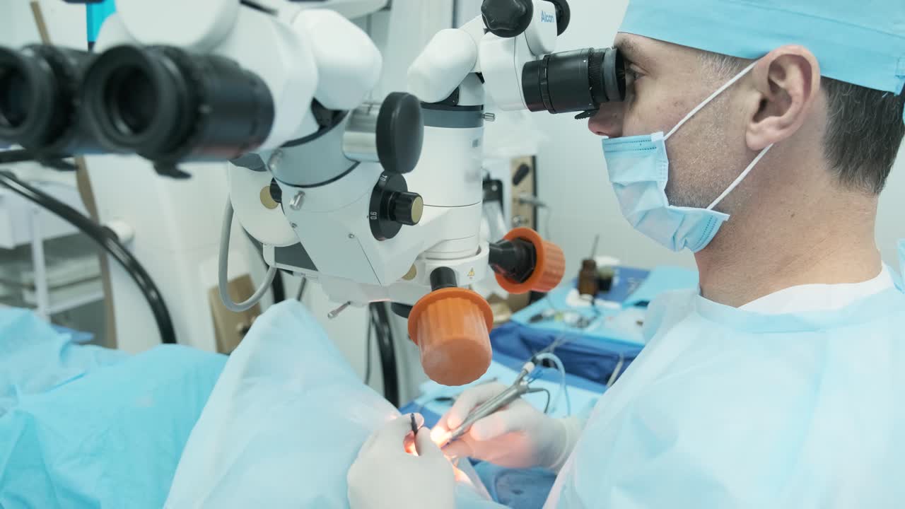 Surgeon looking into the microscope at the eye of female patient at the operating room. Doctor using microscope during eye surgery process, treatment of cataract and diopter correction.