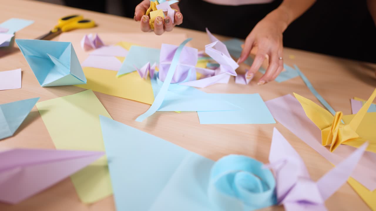 Primo piano di mani che piegano e dispongono meticolosamente diverse forme colorate di carta origami sul legno