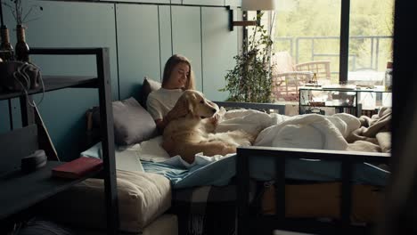 The-blonde-girl-lies-on-the-bed-with-her-dog-and-strokes-her.-Peace-and-harmony-with-your-pet