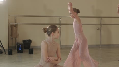 a group of young ballet students in black dancewear practicing positions in a spacious ballet studio with wooden flooring and wall-mounted barres. focused expressions and synchronized movements.