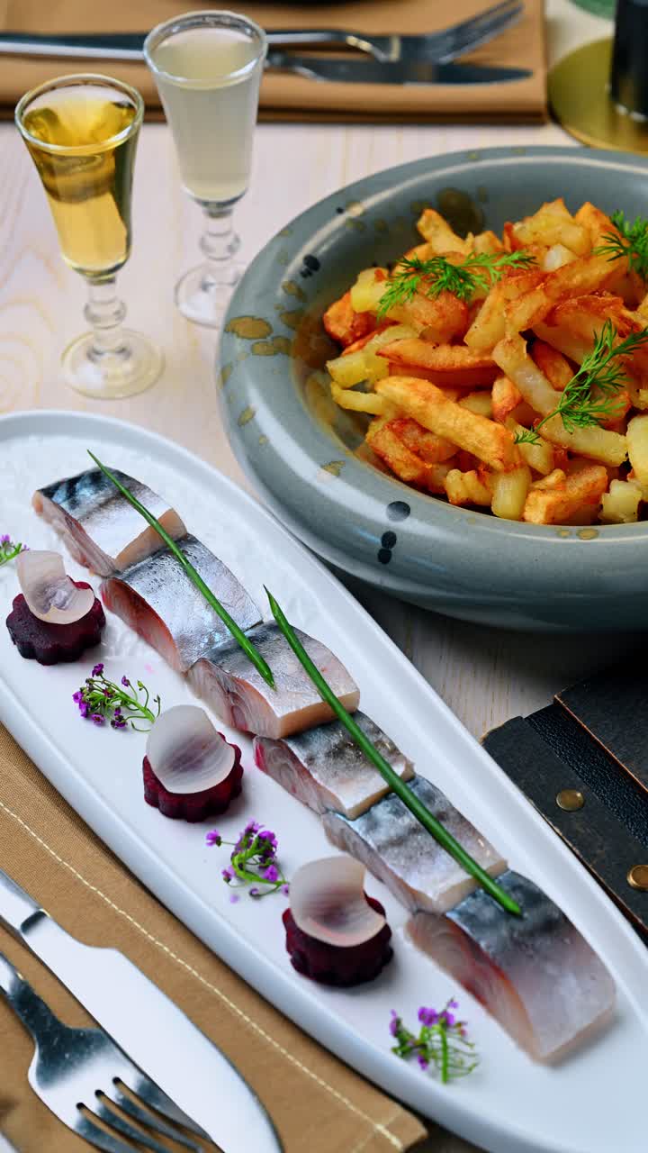 Gourmet herring appetizer with side of crispy fried potatoes. Salted fish slices served with beetroot rounds and a side of golden potato wedges on a restaurant table
