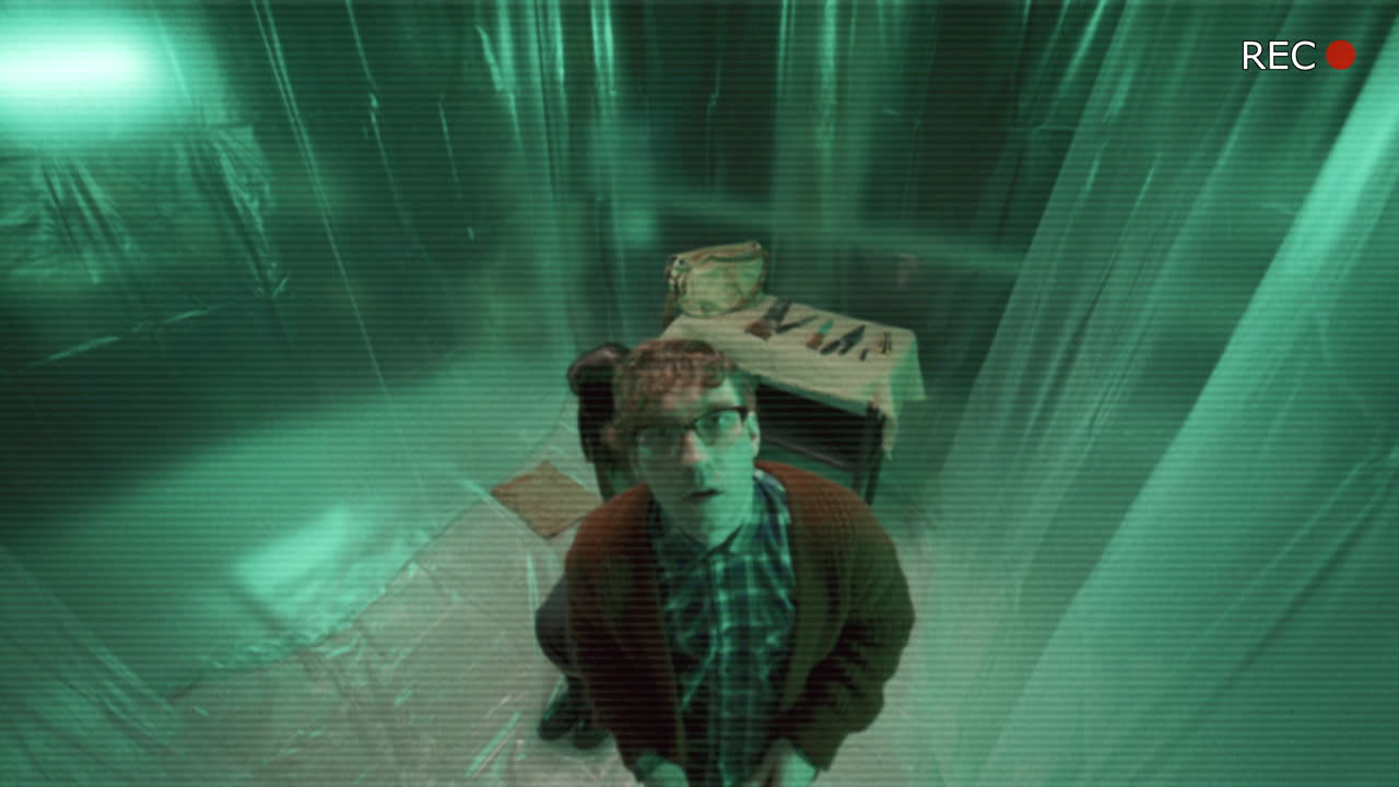 imágenes de cctv de un asesino en serie amenazando a un rehén en una habitación cubierta de plástico