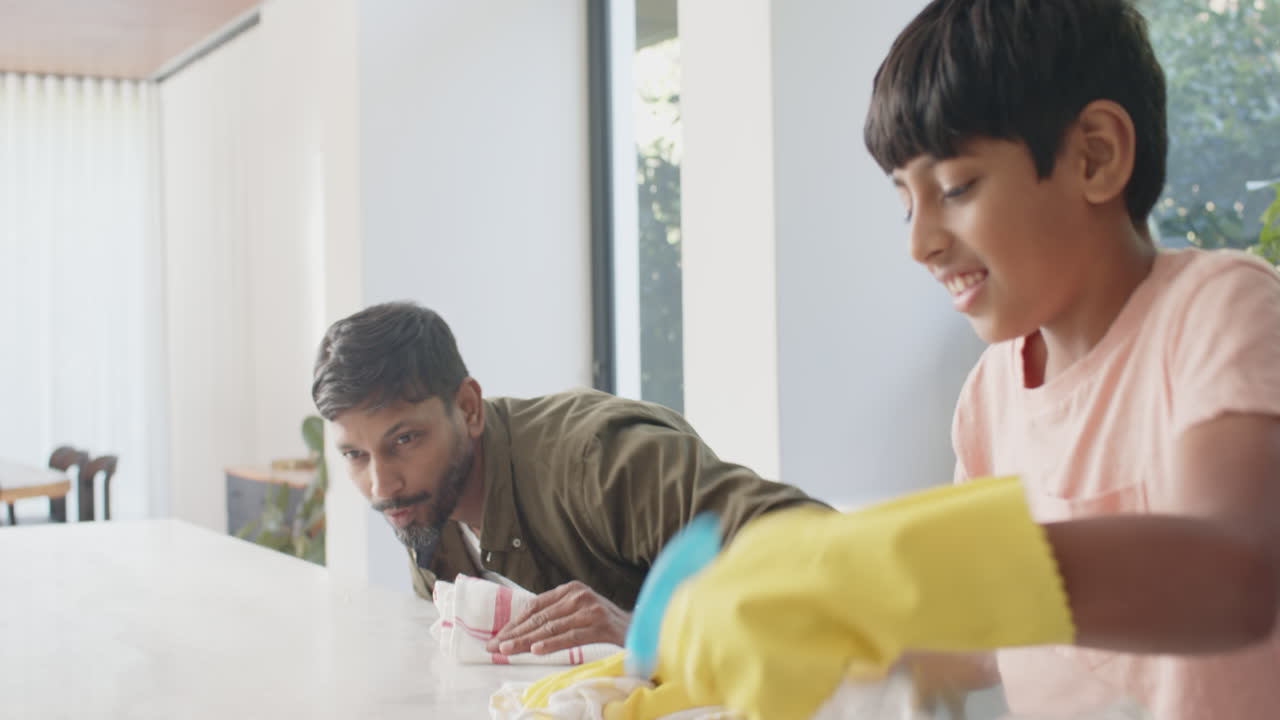 Cleaning kitchen counter, Indian father and son wearing gloves and using spray bottle