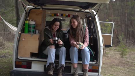 two young girl friends chat in the back of a caravan in the middle of the forest.