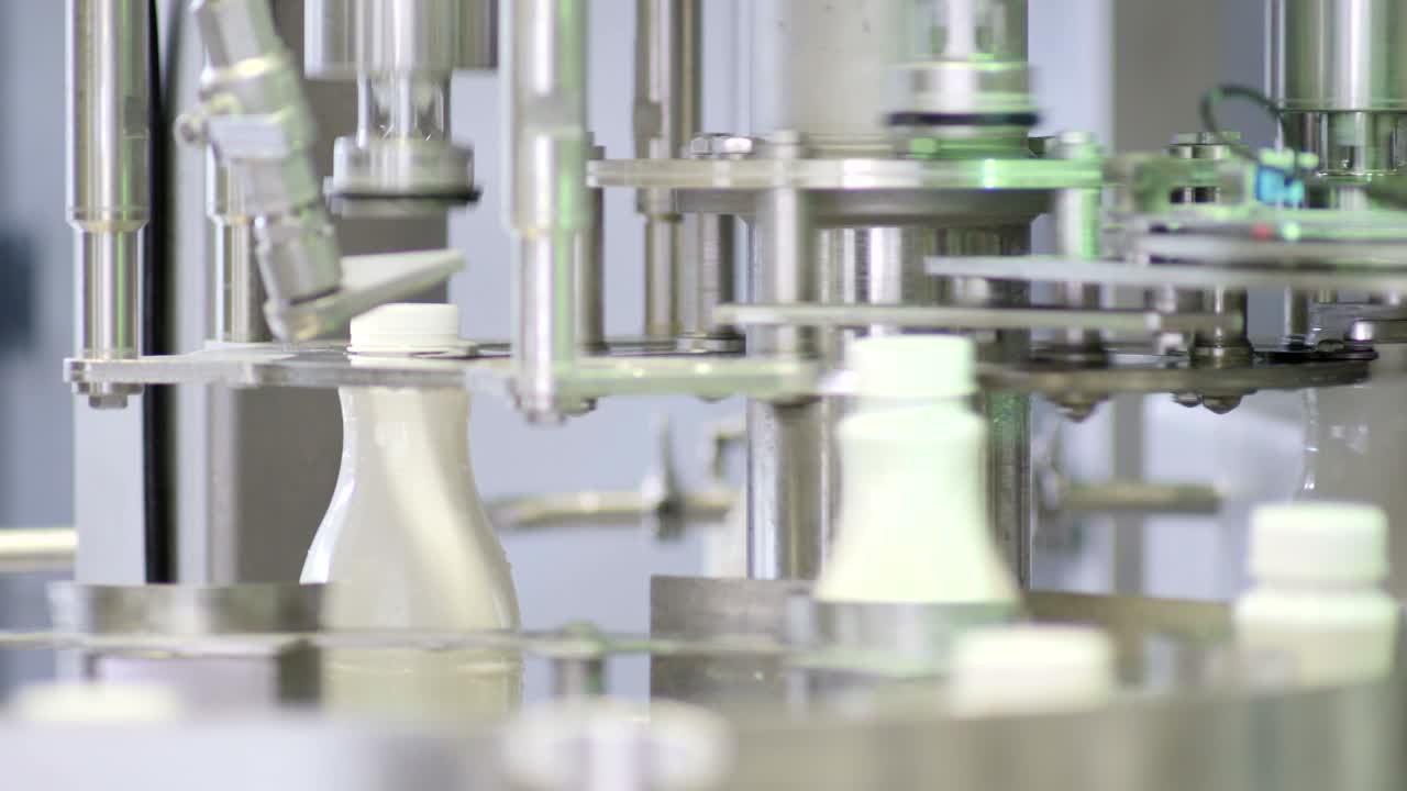 우유 회사에서 생산 라인에서 색 플라스틱 우유 병의 영상, 병이 채워지고 봉인됩니다.