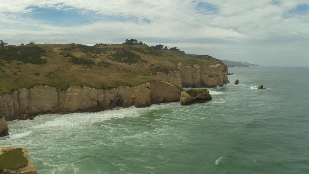 Aerial zooming out orbiting shot of cliffs along the coast in New Zealand during the day