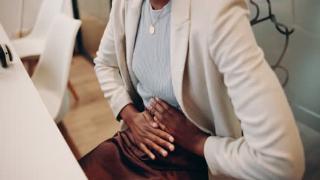 a woman in a white blazer and brown skirt sits at a desk, holding her stomach in pain