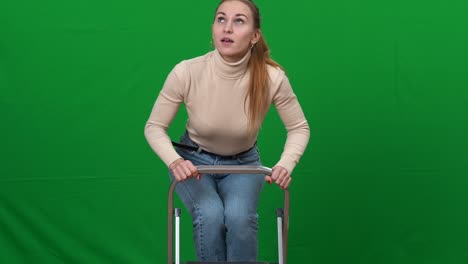 mujer caucásica subiendo la escalera tratando de alcanzar algo en la parte superior. retrato de una joven delgada preocupada reparando reparando en pantalla verde fondo chromakey