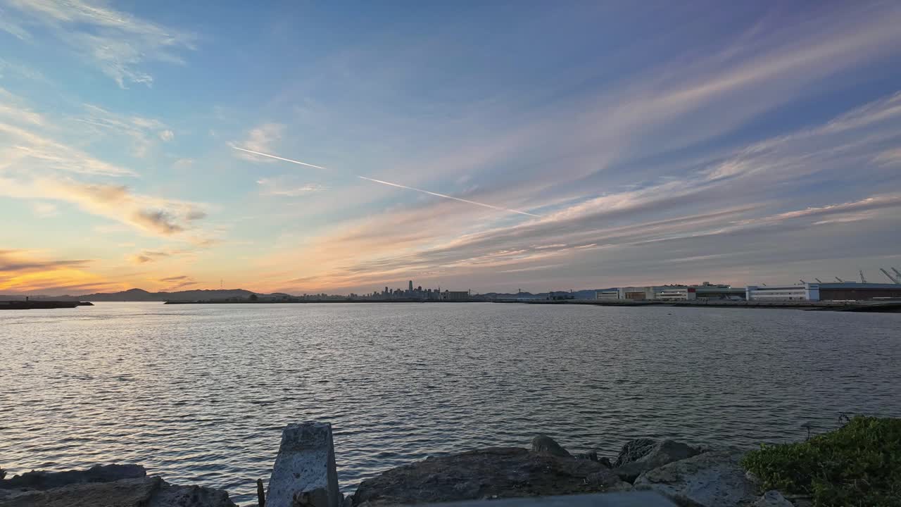 A dynamic left-to-right time-lapse of Alameda Waterfront Park, capturing the tranquil bay waters, lush greenery, and the gentle motion of boats against a vibrant California sky.