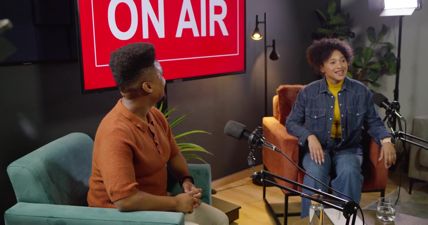 Afroamerikanske værter diskuterer i mikrofoner til live podcast i studie efter at have trykket på en tablet.
