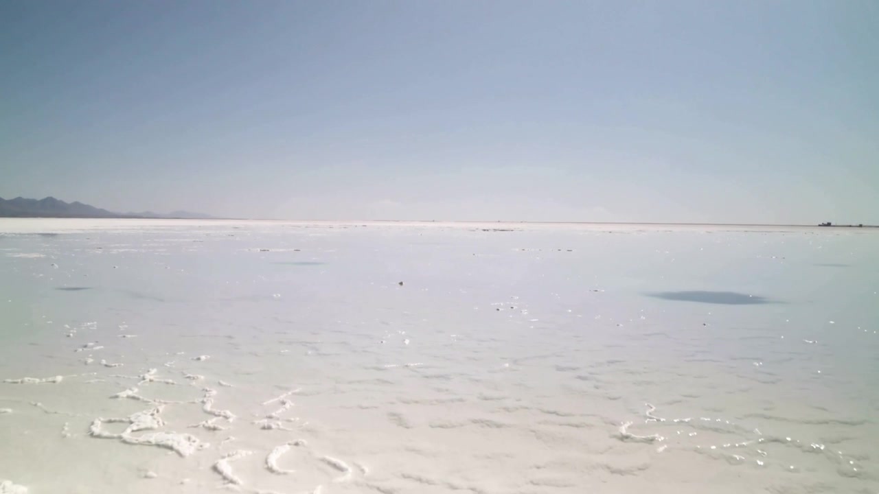 Displaying broad salt-encrusted ground shimmering under bright sun on salt flat, with shallow pools