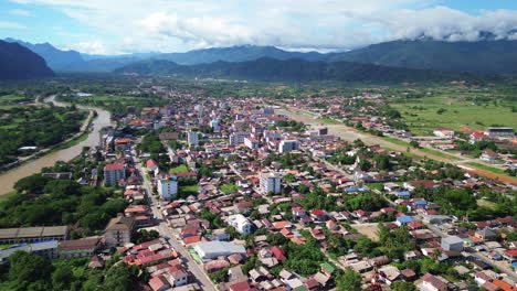 Aerial establish of Vang Vieng town surrounded by limestone mountains and lush green fields, panoramic overview at midday