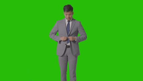 three quarter length portrait of businessman straightening suit against green screen