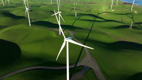 orbiting around wind turbine spinning in slow motion against green hills at wind turbine farm, northern california