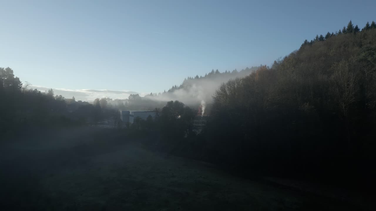 White smoke rising from a factory in sant hilari sacalm, catalonia, early in the morning, creating a mystical atmosphere as it mixes with the fog covering the valley
