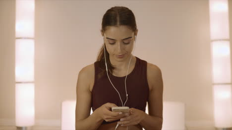 girl sitting in lotus pose on mat. woman in earphones using smartphone in studio