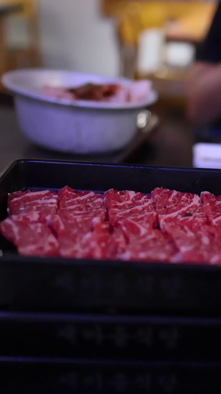 Potret close-up vertikal irisan daging sapi mentah marmer yang ditumpuk di atas nampan hitam di sebuah restoran.