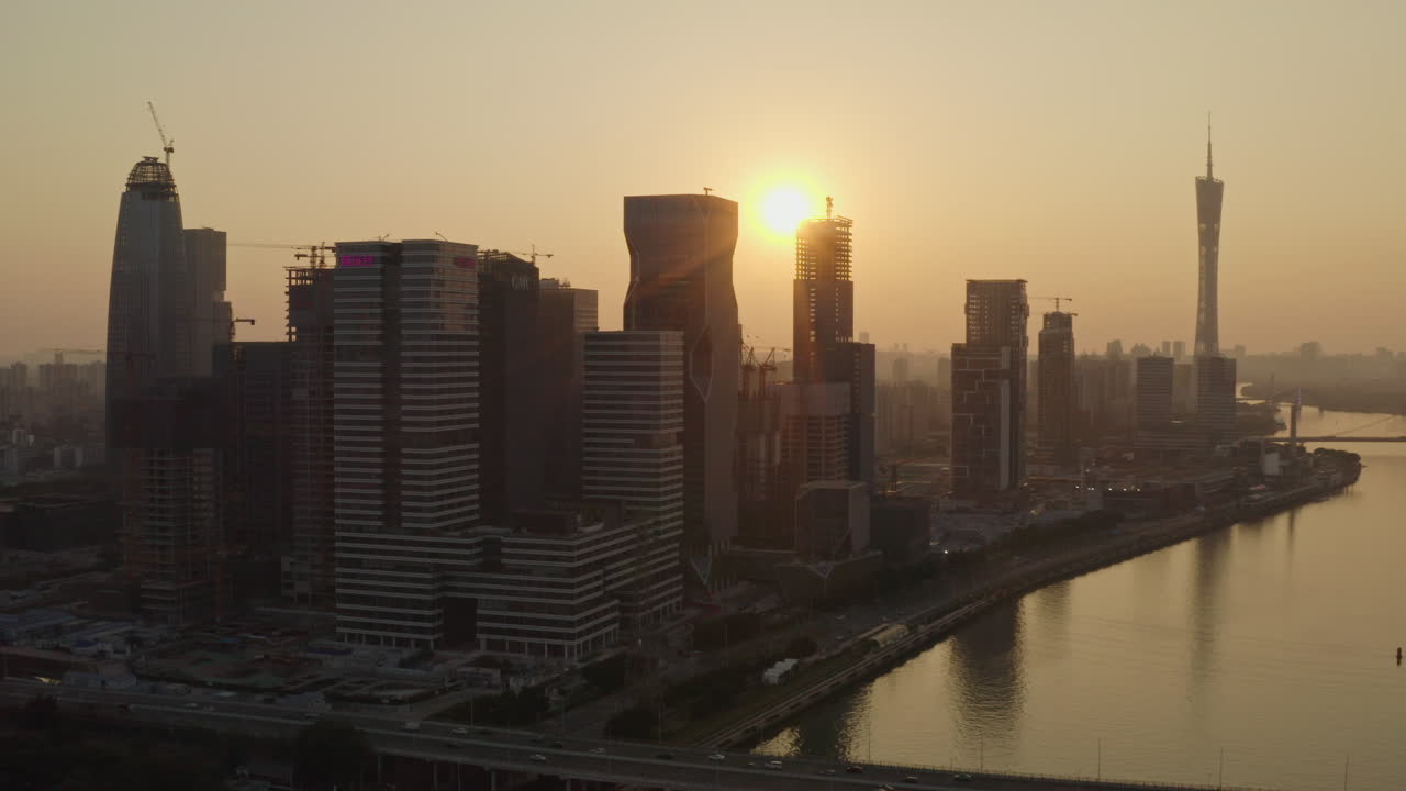 Giro lento em torno do canteiro de obras do distrito de edifícios de escritórios do Grupo Alibaba na margem do Rio das Pérolas, ao pôr do sol dourado e colorido, com a Torre de Cantão ao longe