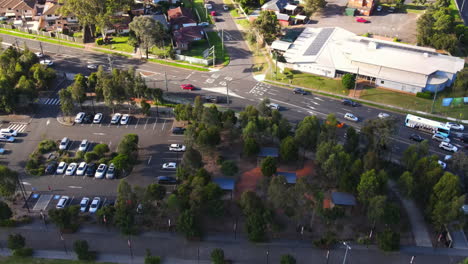 Busy-streets-in-suburban-community-with-cars-and-bus-near-homes,-field-and-businesses