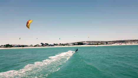 Tiro-De-Drone-Ultra-Ancho-Persiguiendo-A-Un-Surfista-De-Cometas-A-Toda-Velocidad-En-El-Hermoso-Sol-De-Luz-Natural-Con-Cielo-Azul-En-La-Playa-De-Langebaan,-Ciudad-Del-Cabo,-Sudáfrica-Con-Paisaje-De-Playa-De-Vacaciones-De-Verano