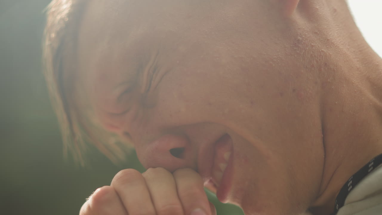 햇빛이 비치는 보케와 함께 땀을 흘리고, 불안해하며 야외에서 클로즈업으로 촬영한 백인 남성의 초상화. 랩 사이에서 멈춰 선 러너, 입술을 깨무는 학생, 장면을 되돌아보는 배우, 눈에 보이는 피부 텍스처, 땀방울을 보여줍니다.