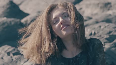 brown haired woman enjoys sunlight and wind on old rocks