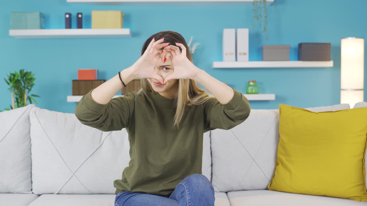 귀여운 젊은 소녀가 행복하게 카메라에 심장 기호를 만들고 있습니다.