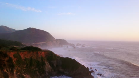 Bixby-Creek-Brücke-Big-Sur-Kalifornien-Luftaufnahmen-Filmisch-Drohne-Flug-Pazifischer-Ozean-Nor-Cal-Winter-Sommer-Große-Welle-Swell-Krachend-Schroffe-Küste-Nachmittag-Goldene-Stunde-Rosa-Sonnenuntergang-Rückwärtsbewegung