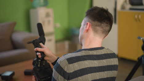 man adjusting camera or filming equipment in creative space with yellow cabinet and green wall in background. focused on task, preparing for content creation or filming in modern home studio