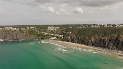 Bird's-eye-view-of-a-beautiful,-calm-bay-with-turquoise-water-surrounded-by-rugged-cliffs-and-white-villas