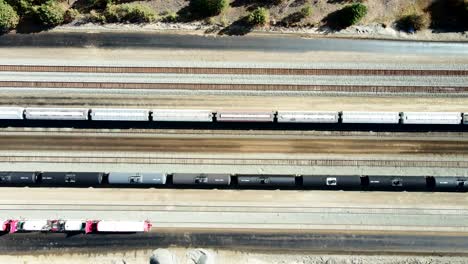 bird's-eye view truck sideways drone shot flying over railroad station in a desert environment on a sunny day with cargo and tank tain