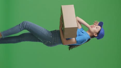 side view of tired asian female courier in blue uniform walking and swiping sweat while delivering a carton on green screen background in the studio