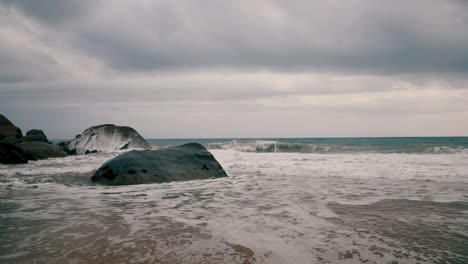 Slow-motion-water-splashing-on-the-rocks-in-a-seashore-on-a-cloudy-day-with-blue-sea