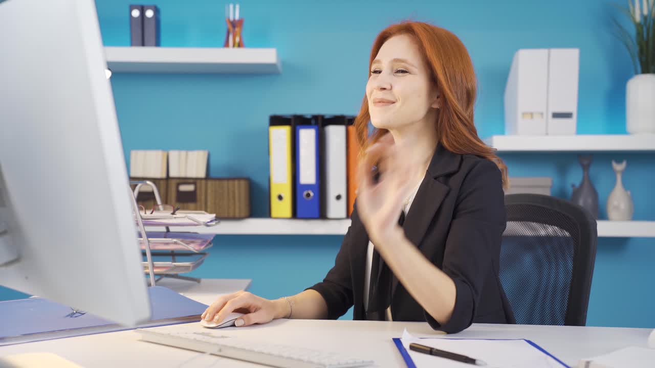 A business woman doing work from the computer turns to the camera and makes the 'VERY GOOD' sign.