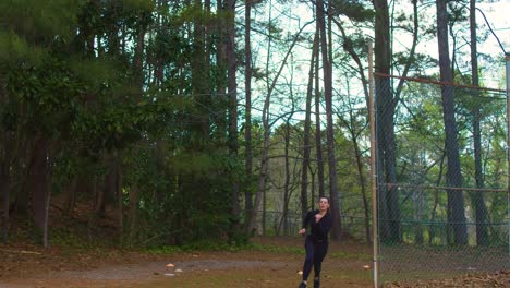 A-young-woman-sprints-from-behind-a-backstop-while-exercising-in-a-wooded-park