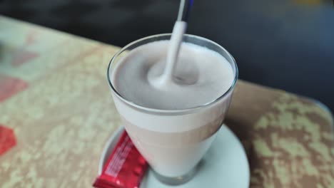 a spoon gently stirs frothy hot cocoa in a glass, creating a smooth swirl, cafe