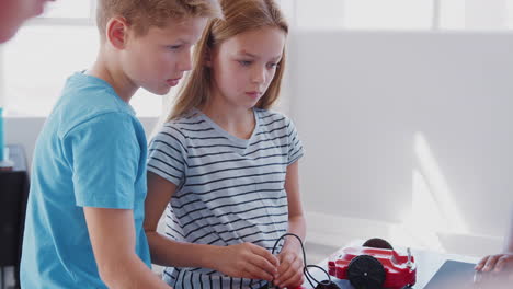 group of students in after school computer coding class learning to program robot vehicle