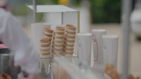 servidor scooping helado en un cono, con pilas de conos y dispensadores en el fondo