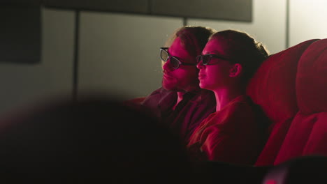 vista lateral de una pareja con gafas 3d sentada en el cine mientras ven una película y comen palomitas de maíz con las luces apagadas 1