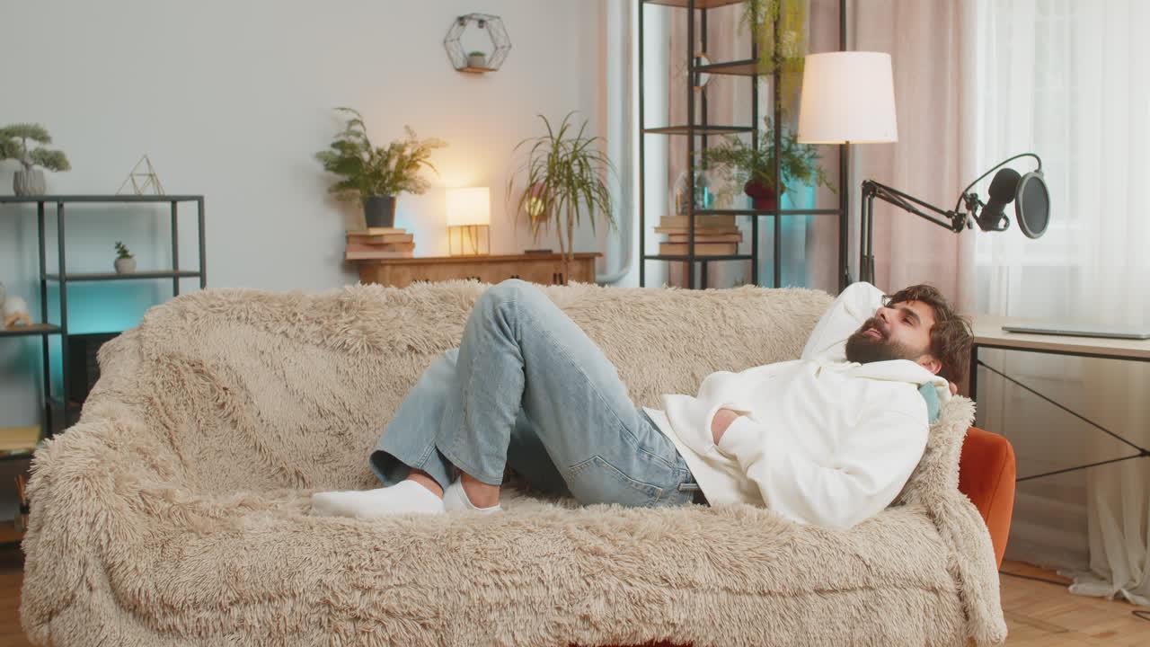 지친 인디언 잘생긴 젊은 남자는 집 아파트의 거실에서 소파에 누워 휴식을 즐기고 있습니다.