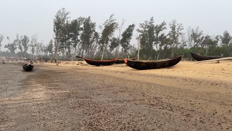 Toma-En-Gran-Angular-De-Muchos-Barcos-Pesqueros-Mantenidos-En-Una-Playa-Silenciosa-Y-Vacía-Durante-El-Día-Con-Algunos-árboles-Detrás-De-Ellos-En-Bengala,-India