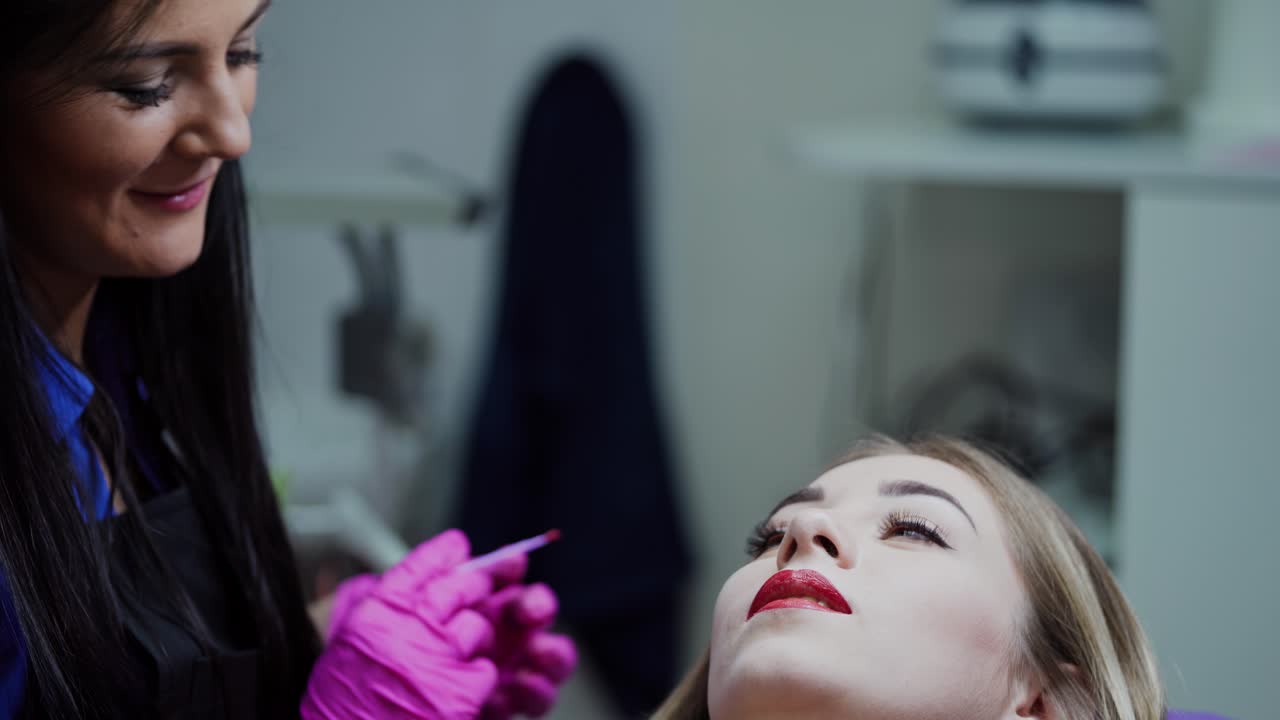 Beautician doing permanent makeup on lips. Skilled cosmetologist woman applying cosmetic procedure on patient's lips in modern spa salon.